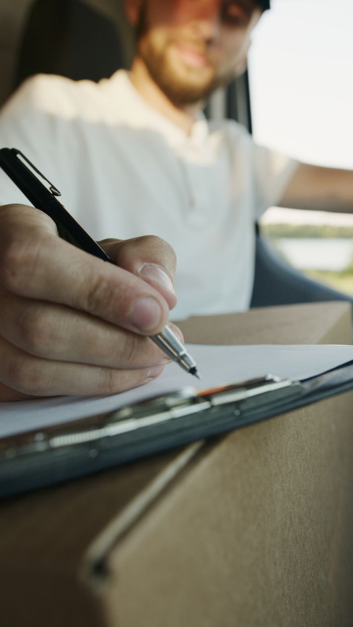 Crafting Captivating Headlines: Your awesome post title goes here Close-up of a delivery driver writing on a clipboard while holding a package inside a vehicle.